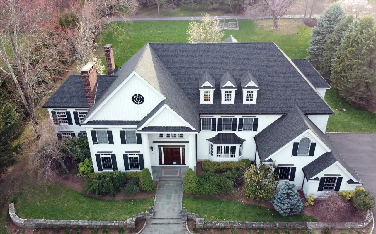 Aerial view of a large white house with a dark shingle roof